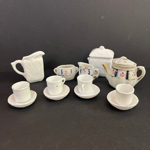 Peut inclure: Un service à thé en porcelaine blanche avec des motifs floraux bleus et rouges. L'ensemble comprend une théière, un pot à crème, un sucrier, quatre tasses et quatre soucoupes.
