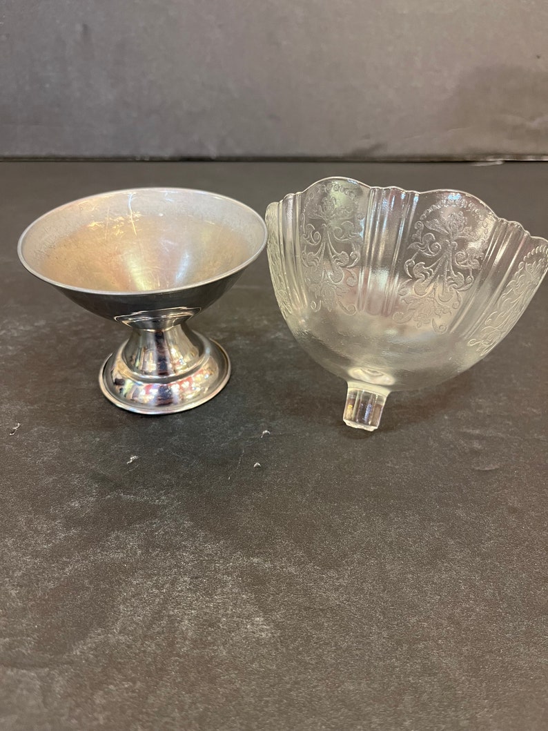 Peut inclure: Deux petits bols, l'un en argent et l'autre en verre transparent avec un motif d&eacute;coratif. Les bols sont sur une surface gris fonc&eacute;.