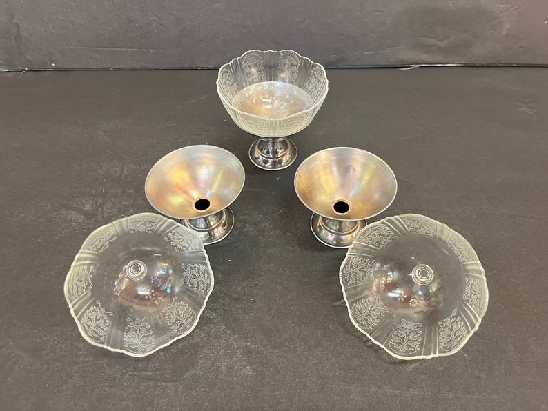 Peut inclure: Quatre coupelles &agrave; dessert en verre transparent avec des bases argent&eacute;es. Les coupelles ont un bord festonn&eacute; et un motif floral d&eacute;licat.