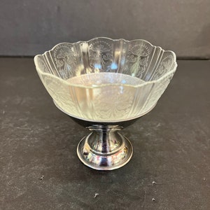 Peut inclure: Un bol en verre transparent avec un motif grav&eacute; d&eacute;coratif repose sur un pied en argent. Le bol a un bord festonn&eacute; et est parfait pour servir des desserts ou des en-cas.