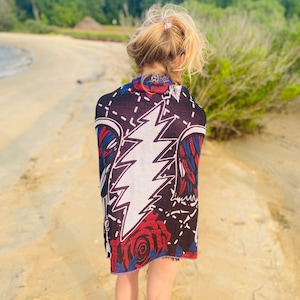 May include: A person wearing a black and red patterned shawl with a white lightning bolt design and a red rose. The shawl is worn over a white shirt.