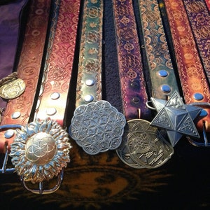 May include: A collection of eight leather belts with intricate designs and metal buckles. The belts are arranged in a row, with the buckles facing the viewer. The buckles are all different shapes and sizes, and some have a flower or geometric pattern.