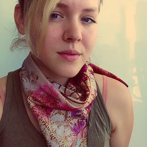 May include: A woman with blonde hair is wearing a green tank top with the word "ORIGINAL" printed on it. She is wearing a pink and gold patterned scarf around her neck.