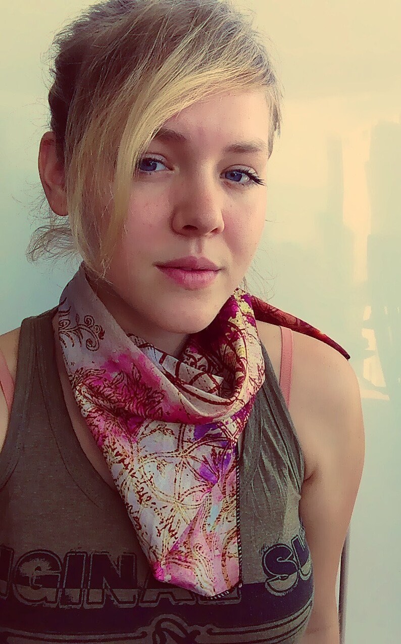 May include: A woman with blonde hair is wearing a green tank top with the word "ORIGINAL" printed on it. She is wearing a pink and gold patterned scarf around her neck.