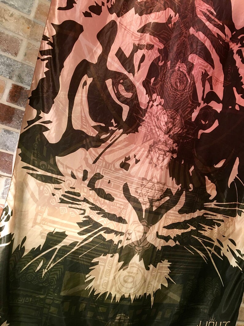 May include: A fabric with a tiger face design. The tiger's face is depicted in black and brown against a light pink and beige background. The design includes intricate patterns and details, creating a striking visual.