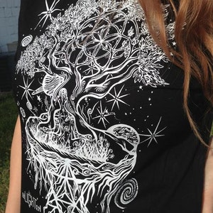 Pode incluir: Camiseta preta com um gr&aacute;fico branco de uma &aacute;rvore com ra&iacute;zes e galhos intrincados. A &aacute;rvore &eacute; cercada por estrelas e uma lua crescente. O texto "all light" &eacute; vis&iacute;vel na parte inferior do design.