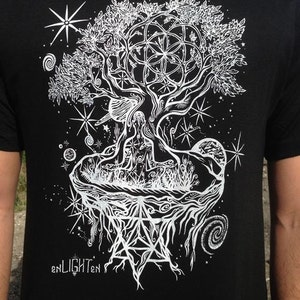 May include: Black t-shirt with a white graphic design of a tree with roots, branches, and leaves. The tree is surrounded by stars and other celestial symbols. The text "enLIGHTen" is at the bottom of the design.