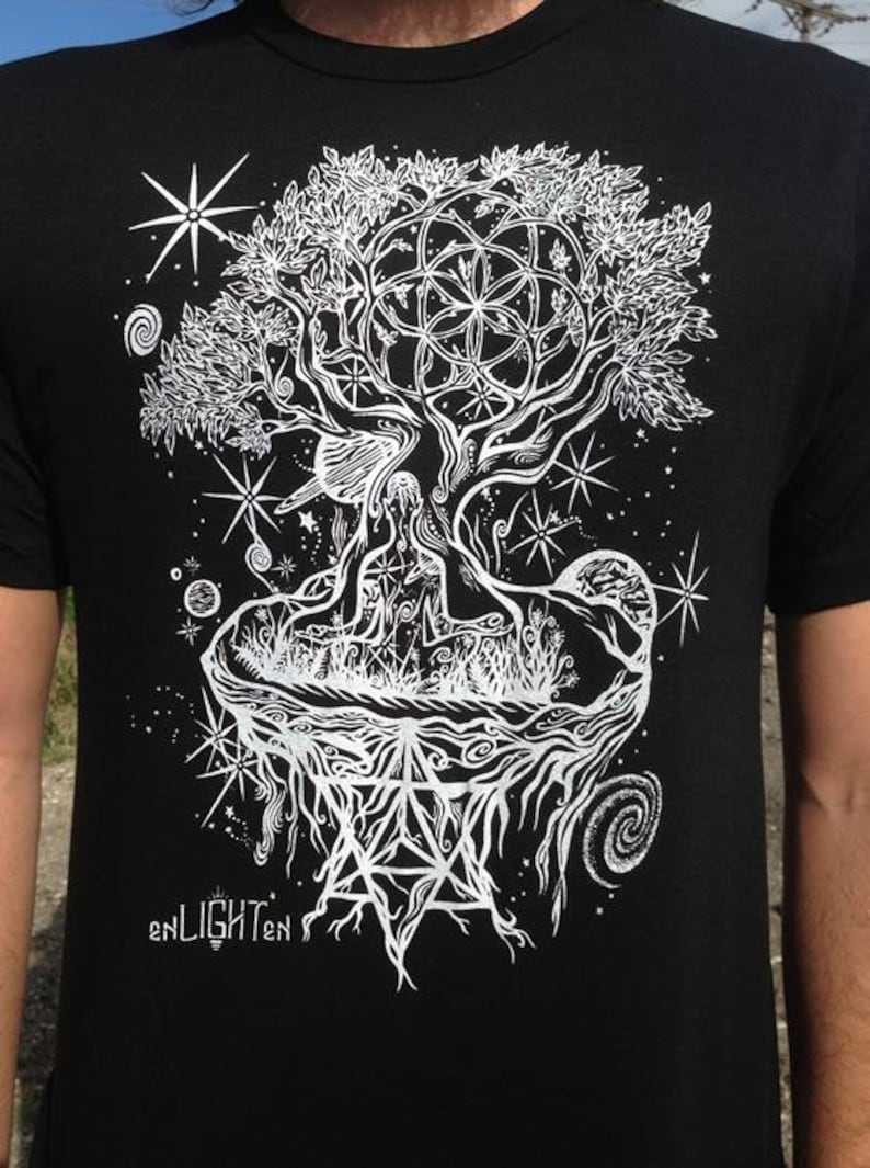 Pode incluir: Camiseta preta com um design gr&aacute;fico branco de uma &aacute;rvore com ra&iacute;zes, galhos e folhas. A &aacute;rvore &eacute; cercada por estrelas e outros s&iacute;mbolos celestiais. O texto "enLIGHTen" est&aacute; na parte inferior do design.