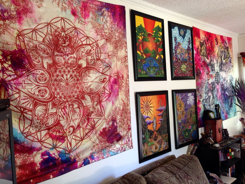 May include: A room featuring wall art and tapestries. A large tapestry with a red geometric design hangs on the left. Several framed art pieces with colorful landscapes are displayed, along with a vibrant tapestry on the right.