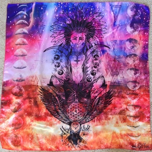 May include: A square scarf with a vibrant, colourful design. The artwork features a Native American figure with a feathered headdress, surrounded by celestial elements like moons and geometric shapes. An eagle is at the bottom, with a flower of life symbol.