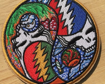 May include: A circular embroidered patch with a colorful design featuring a skull, lightning bolts, and a swirling pattern. The patch is surrounded by a gold border.