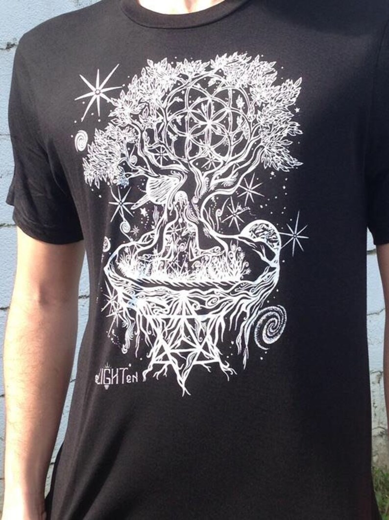 Pode incluir: Camiseta preta com um gr&aacute;fico branco de uma &aacute;rvore com detalhes intrincados, incluindo um design de flor da vida, estrelas e um padr&atilde;o geom&eacute;trico. O texto "Enlighten" &eacute; vis&iacute;vel na parte inferior do design.