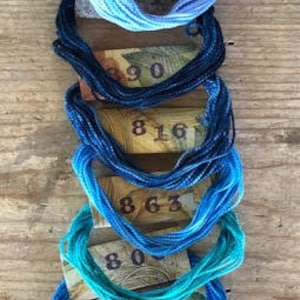 May include: A collection of 10 spools of DMC embroidery floss in shades of blue, teal, and navy. The spools are labeled with DMC numbers: 817, 815, 890, 816, 863, 807, 815, 809, 3813, and 3817.