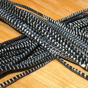 Pode incluir: Close-up de um feixe de cordas listradas em preto e branco. As cordas estão dispostas em um padrão emaranhado, com as listras criando um contraste visual marcante. As cordas parecem ser feitas de um material flexível.