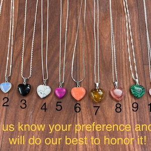 May include: Eleven silver necklaces with heart-shaped pendants made of different colored stones. The stones are green, white, black, white and black, pink, orange, yellow, pink, green, pink, and blue.