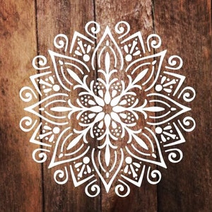 Pode incluir: Design de mandala branco com detalhes intrincados em um fundo de madeira marrom.