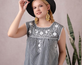 May include: A black and white gingham top with white floral embroidery. The sleeveless blouse has a square neckline and is paired with black pants. The person is wearing a black hat and gold earrings.