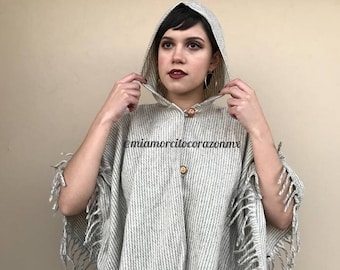 May include: A hooded poncho with a striped pattern and fringe trim. The poncho is made of a soft, warm fabric and is perfect for layering in the fall or winter. The poncho is a light gray color with white stripes.