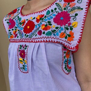 Peut inclure: Un chemisier sans manches en vichy violet et blanc avec une broderie florale color&eacute;e autour de l'encolure.