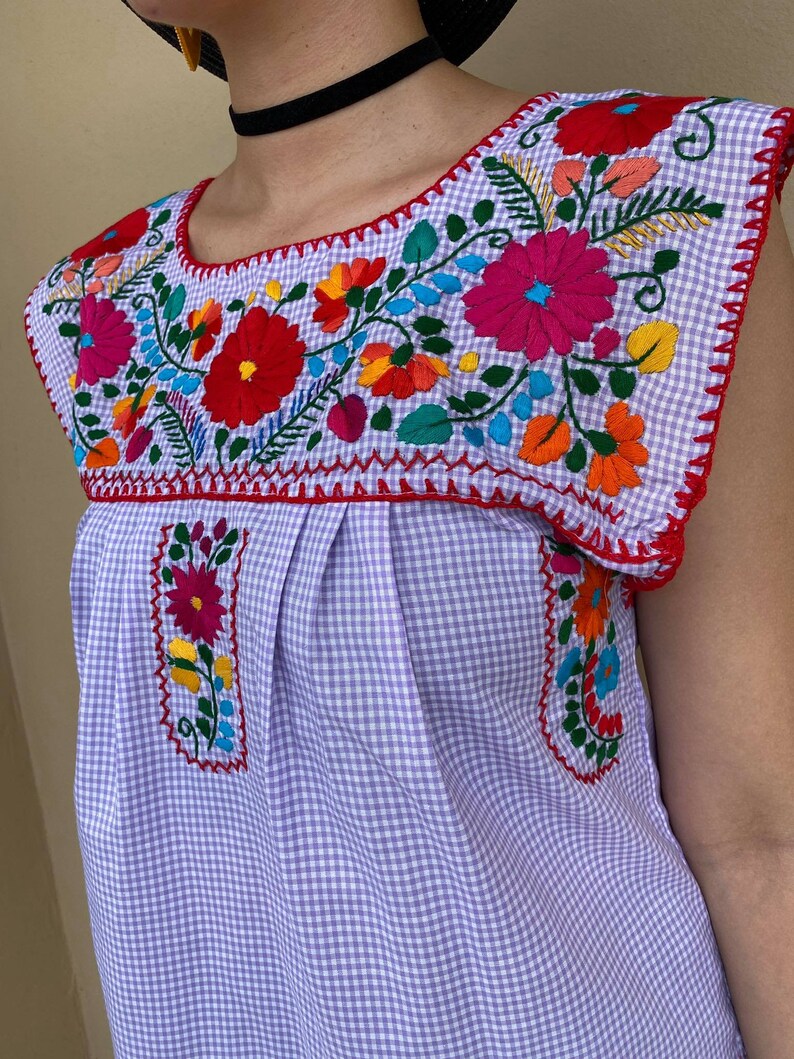 Peut inclure: Un chemisier sans manches en vichy violet et blanc avec une broderie florale color&eacute;e autour de l'encolure.