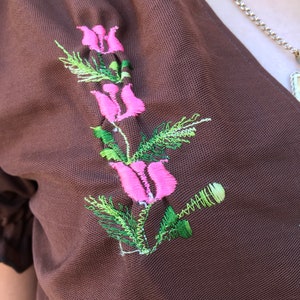 May include: A brown fabric garment with a pink and green embroidered flower design.
