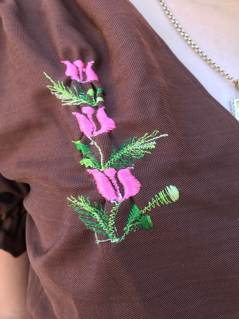 May include: A brown fabric garment with a pink and green embroidered flower design.