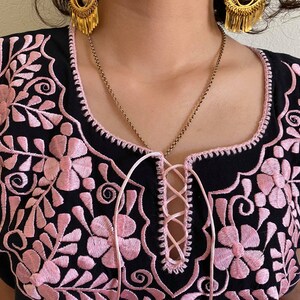 May include: Black embroidered blouse with pink floral details and a lace-up neckline.