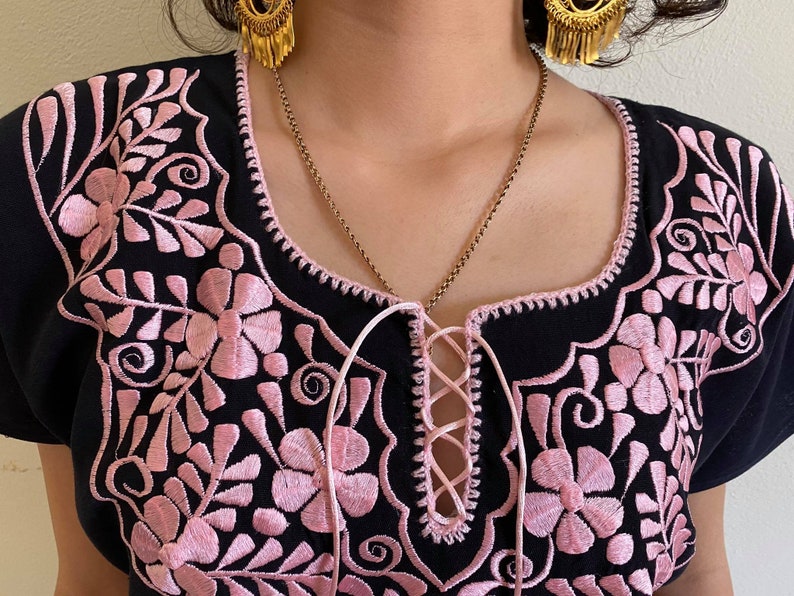 May include: Black embroidered blouse with pink floral details and a lace-up neckline.