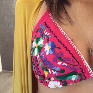 May include: A pink embroidered bikini top with colorful floral designs. The top has a white crocheted trim.