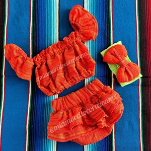 Op de afbeelding: Oranje-wit gestreept baby-outfit met een bijpassend hoofdband. De outfit bestaat uit een geruit topje en een broekje. Het hoofdband heeft een grote strik.
