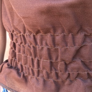 May include: A brown, stretchy fabric with a gathered elastic waistband. The fabric has a subtle texture and a slightly sheen finish.