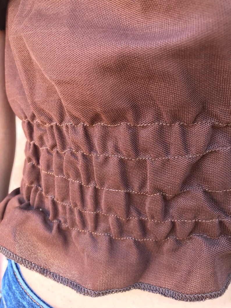 May include: A brown, stretchy fabric with a gathered elastic waistband. The fabric has a subtle texture and a slightly sheen finish.
