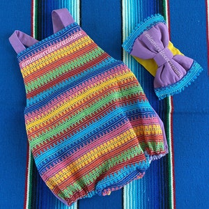 Könnte beinhalten: Ein bunter gestreifter Baby-Strampler mit einem lila Schleifen-Haarband. Der Strampler hat ein Regenbogenmuster und das Haarband hat eine gelbe Basis.