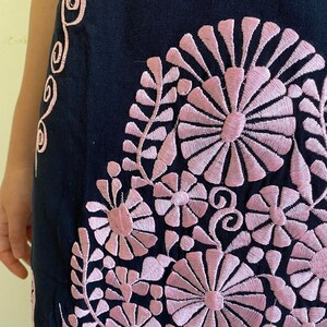 May include: A black skirt with pink embroidered floral designs. The skirt features a variety of flowers and leaves, all stitched in a delicate pink thread.
