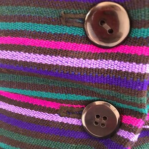 May include: Close-up of a striped fabric with two black buttons. The fabric is brown, purple, pink, and green.