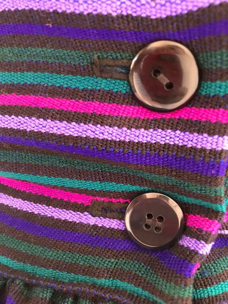 May include: Close-up of a striped fabric with two black buttons. The fabric is brown, purple, pink, and green.