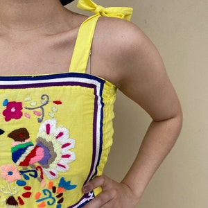 May include: Yellow sleeveless dress with colorful embroidered flowers and a bow on the strap.