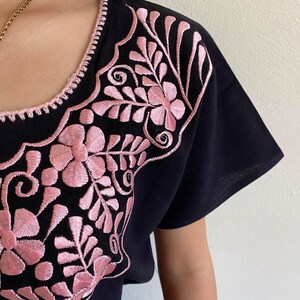 May include: Black short-sleeved shirt with pink floral embroidery around the neckline.