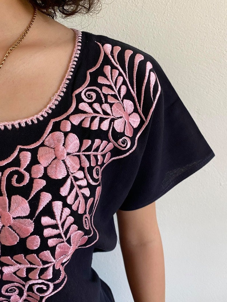 May include: Black short-sleeved shirt with pink floral embroidery around the neckline.