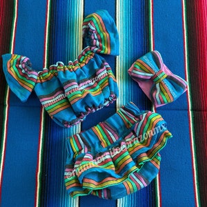 May include: A colorful striped baby outfit with a matching headband. The outfit includes a short-sleeved top and a ruffled skirt. The headband is tied in a bow.