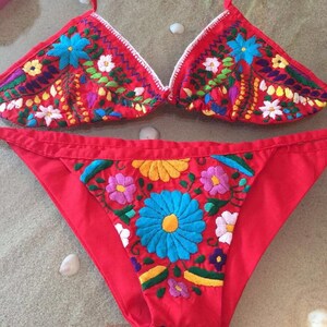 May include: Red bikini with colorful floral embroidery. The top is a triangle style and the bottom is a high-cut style.