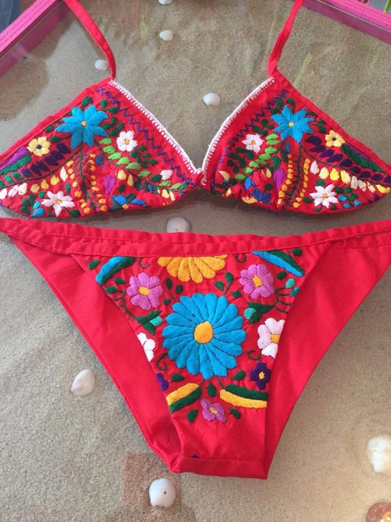 May include: Red bikini with colorful floral embroidery. The top is a triangle style and the bottom is a high-cut style.