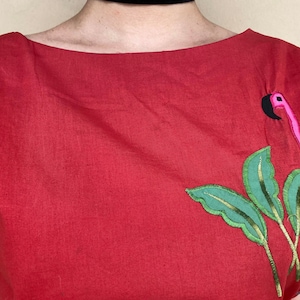May include: Red linen shirt with a pink flamingo and green leaves embroidered on the right side.