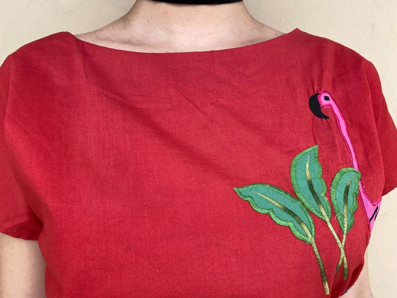 May include: Red linen shirt with a pink flamingo and green leaves embroidered on the right side.