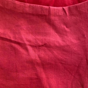 May include: A close-up of a red fabric with a small hole in the center. The fabric has a smooth texture and a slight sheen.