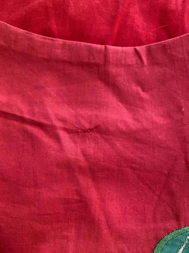 May include: A close-up of a red fabric with a small hole in the center. The fabric has a smooth texture and a slight sheen.