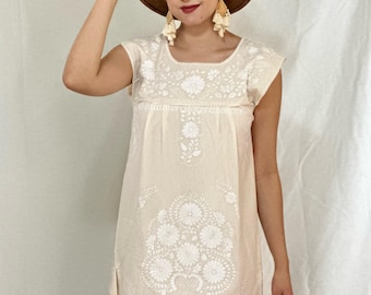 May include: A white cotton dress with white embroidery featuring floral designs. The dress has a square neckline and short sleeves.