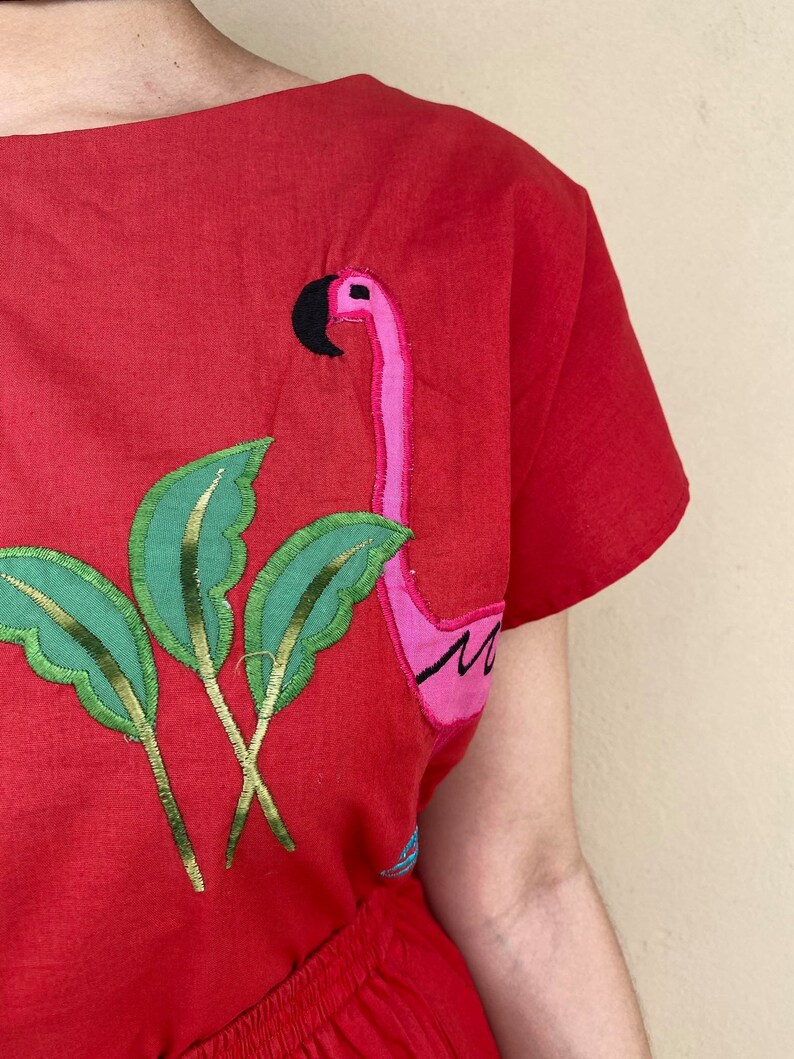 May include: Red cotton dress with embroidered pink flamingo and green palm leaves.