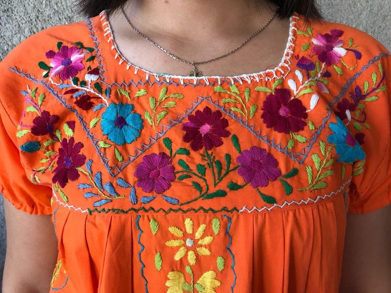 May include: Orange embroidered cotton dress with colorful floral designs. The dress has a round neckline and short sleeves.