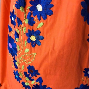 May include: Orange fabric with blue and green embroidered flowers. The flowers are in a floral pattern.